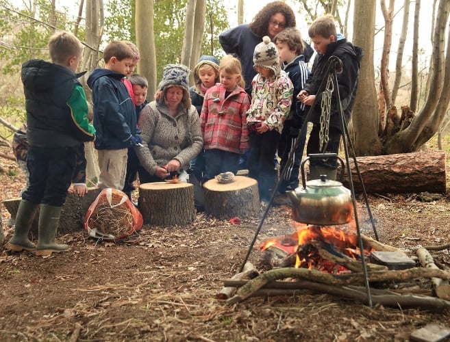 An image of children being shown how to use a fire steel around a fire in the woods at Great Dixter