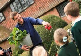 Image of a gardener showing some school children vegetables 